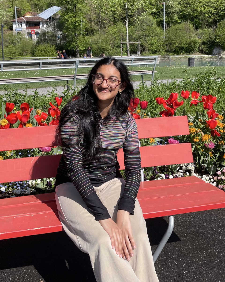 Sukanya Krishna smiling on a red bench in front of tulips